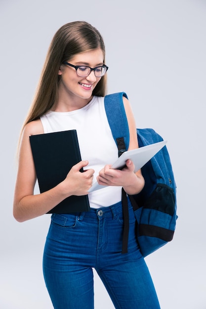 Ritratto di un'adolescente felice con zaino e libro utilizzando un computer tablet isolato su uno spazio bianco