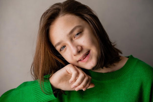 Ritratto di un'adolescente snella in un maglione verde alla luce naturale contro un muro di mattoni bianchi. bellezza naturale, senza trucco. pelle problematica. spazio per il testo. Foto di alta qualità