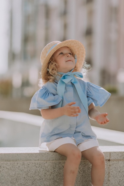 ritratto di un'adorabile bambina bionda in abito blu e cappello di paglia all'aperto