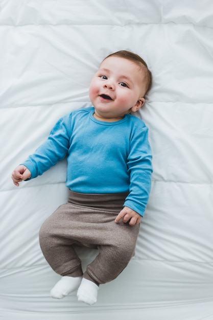 Ritratto di un adorabile bambino di 3 mesi sorridente sdraiato su un letto di lenzuola bianche