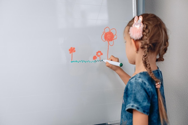 Ritratto di un'affascinante bambina che disegna una piccola immagine su una lavagna bianca con pennarelli. Concetto di sviluppo. foto con rumore