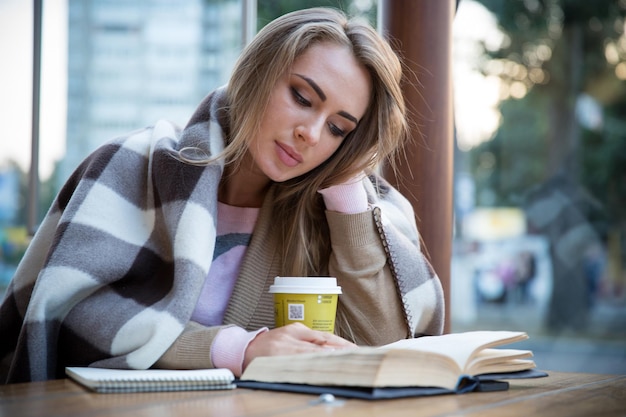 Ritratto di un'affascinante ragazza che legge un libro al caffè