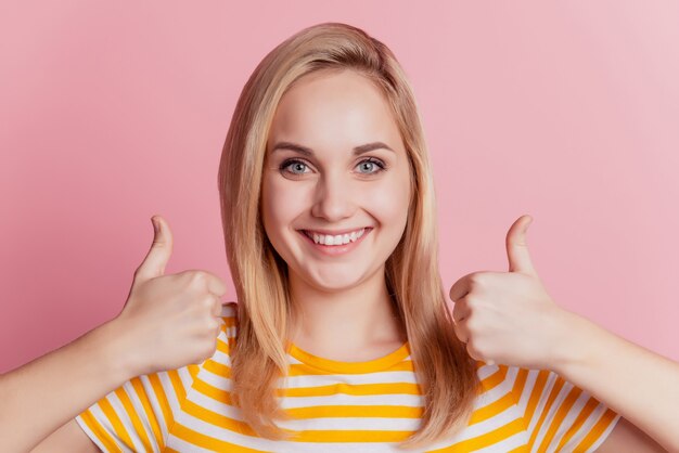 Ritratto di un'affascinante ragazza positiva approva il gesto pollice in su sorriso a trentadue denti su sfondo rosa