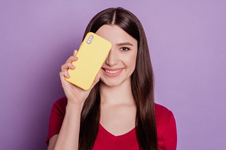 Ritratto di un'affascinante signora positiva che tiene l'occhio della copertina del telefono su sfondo viola