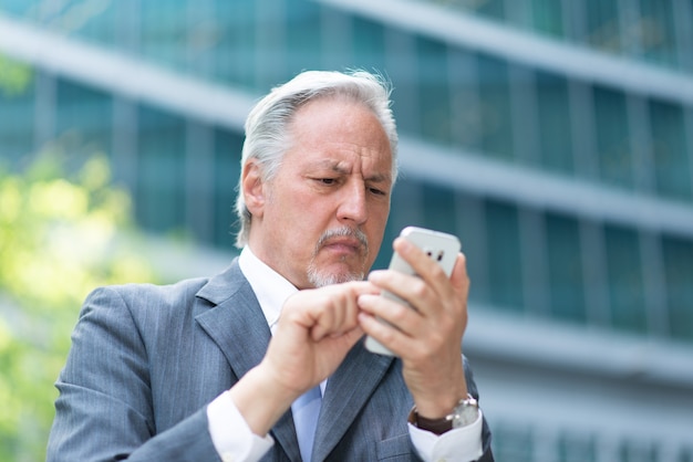 Ritratto di un anziano uomo d'affari che ha un momento difficile durante l'utilizzo del suo telefono cellulare