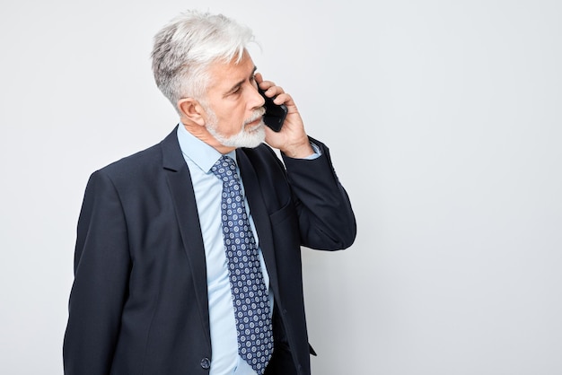 Ritratto di un anziano uomo d'affari in abito che parla al telefono cellulare Una persona con uno smartphone isolato su sfondo bianco