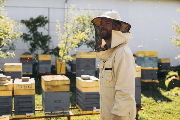 Ritratto di un apicoltore maschio felice che lavora in un apiario vicino ad alveari con api Raccogliere miele Apicoltore su apiario Concetto di apicoltura