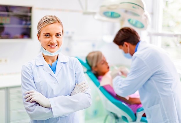 Ritratto di un assistente dentista sorridente mentre il dentista sta lavorando sullo sfondo