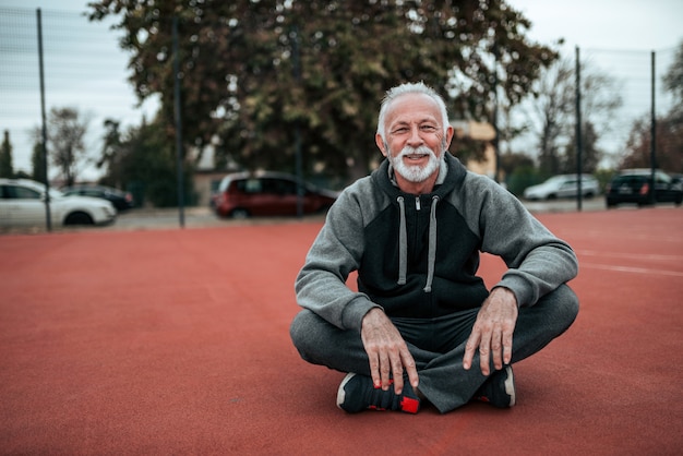 Ritratto di un atleta senior che si siede sulla pista in tartan nello stadio all&#39;aperto.