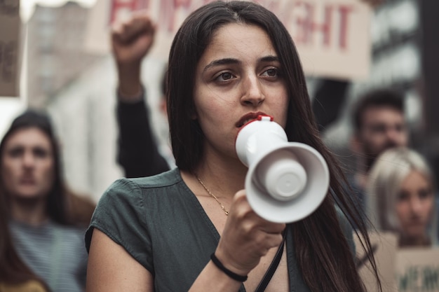 Ritratto di un'attivista donna in una marcia di protesta con in mano un megafono con dei corvi dietro di lei