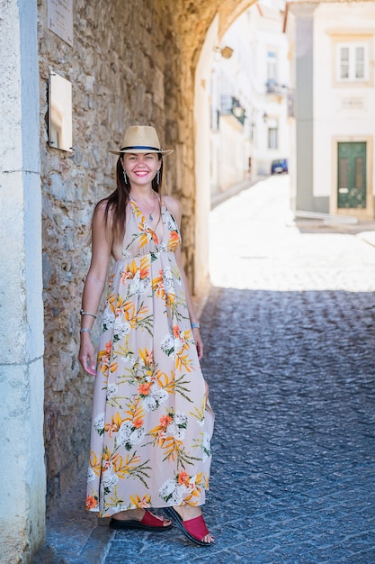 Ritratto di un'attraente donna turistica nella città vecchia Indossando abiti lunghi alla moda, braccialetti e cappello di paglia.