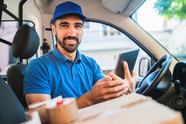 Ritratto di un autista uomo di consegna utilizzando tavoletta digitale mentre era seduto in furgone. Servizio di consegna e concetto di spedizione.