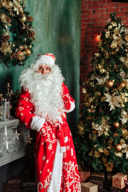 Ritratto di un Babbo Natale emotivo con un sacco di regali vicino al camino di Natale nel soggiorno decorato con l'albero di Natale. Babbo Natale arriva e porta i regali di notte. Copia spazio per il sito