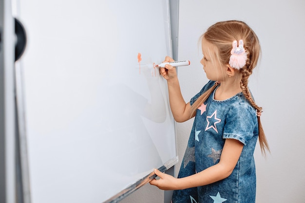 Ritratto di un bambino carino focalizzato in via di sviluppo che fa piccoli disegni su una lavagna bianca con un pennarello arancione. Concetto di disegno. foto con rumore