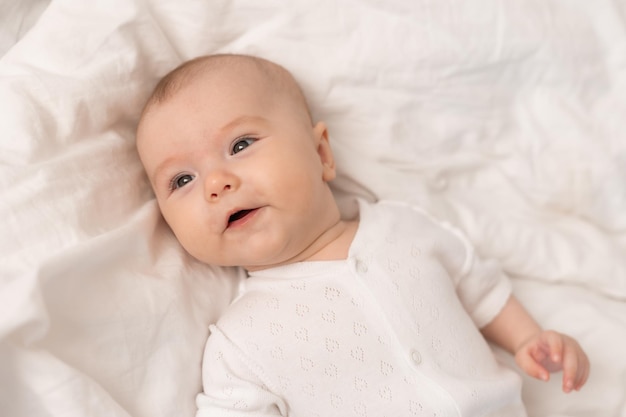 ritratto di un bambino carino in un body bianco su un letto a casa con lenzuola bianche. Neonato a casa