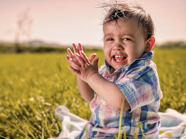 Ritratto di un bambino carino sorridente seduto sul campo contro il cielo