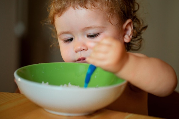 Ritratto di un bambino caucasico carino con un bambino disordinato affamato di cucchiaio con un piatto dopo aver mangiato la purea