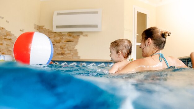 Ritratto di un bambino che ride felice con una giovane madre che gioca con un pallone da spiaggia gonfiabile colorato in piscina al resort estivo dell'hotel