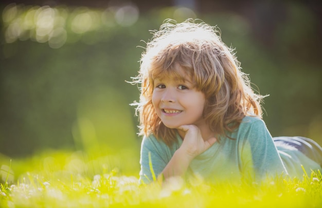 Ritratto di un bambino che ride felice sdraiato sull'erba nel parco naturale estivo. Chiuda sul viso positivo dei bambini.