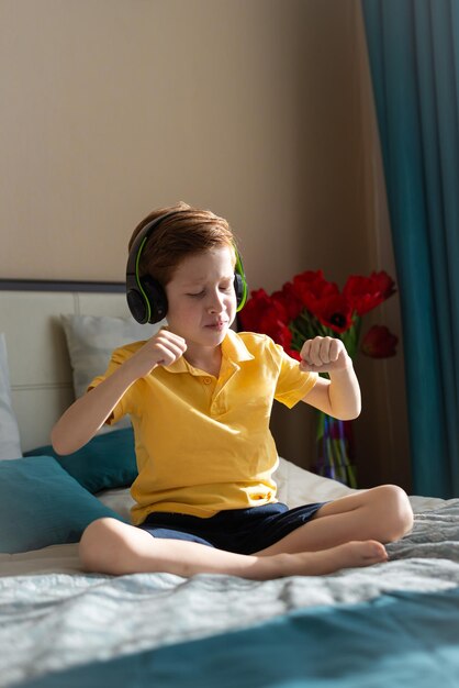 Ritratto di un bambino dai capelli rossi ascolta musica in cuffia felice gode della melodia e balla foto verticale Amante della musica tempo libero e intrattenimento