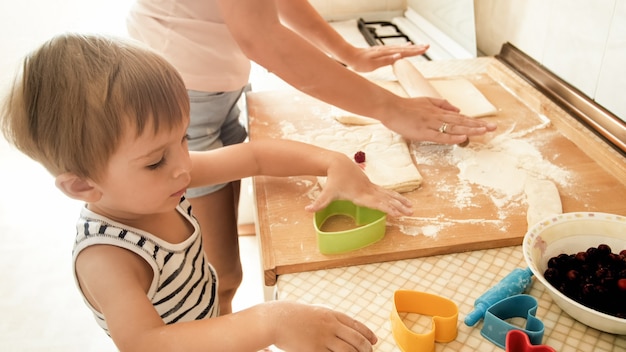 Ritratto di un bambino sorridente felice con la giovane madre che cuoce e cucina in cucina