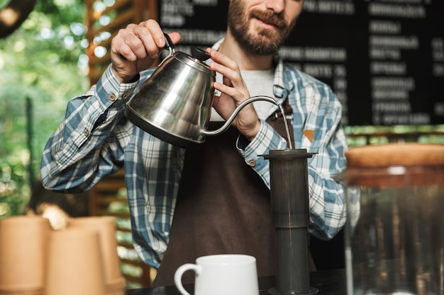 Ritratto di un barista felice che indossa un grembiule che fa il caffè mentre si lavora in un caffè di strada o in un caffè all'aperto