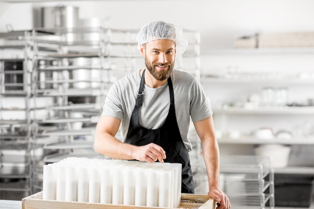 Ritratto di un bel casaro in uniforme che forma il formaggio in stampi presso la piccola azienda agricola