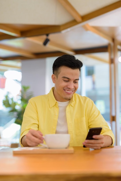 Ritratto di un bel giovane al bar che sorride e usa il cellulare