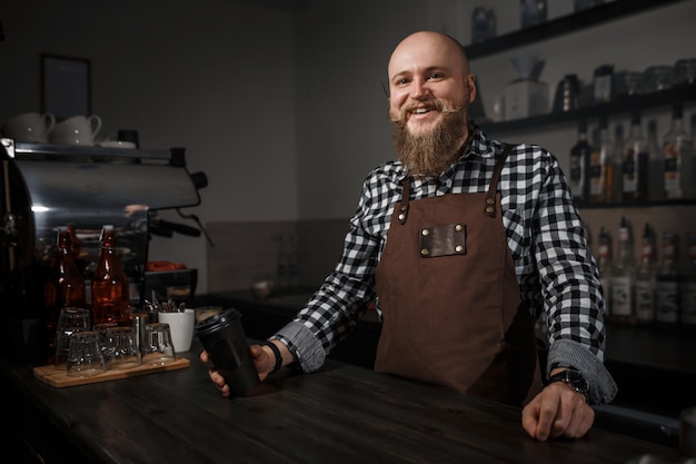 Ritratto di un bel giovane barista in grembiule seduto al bar del moderno caffè