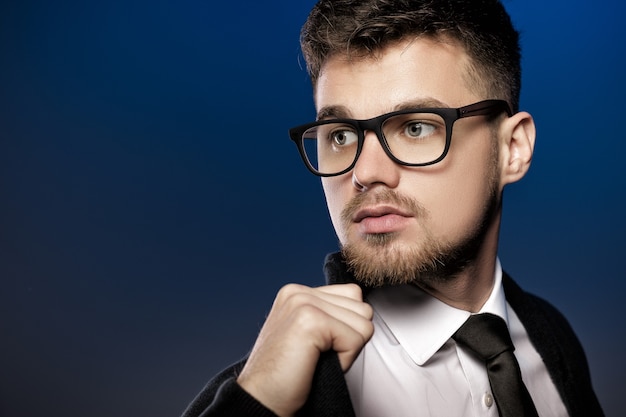 Ritratto di un bel giovane con gli occhiali e una camicia bianca su sfondo blu