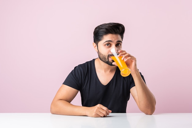 Ritratto di un bel giovane indiano che beve succo d'arancia in cucina al mattino