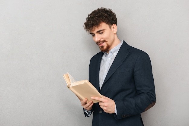 ritratto di un bel giovane uomo d'affari isolato su un libro di lettura muro grigio.