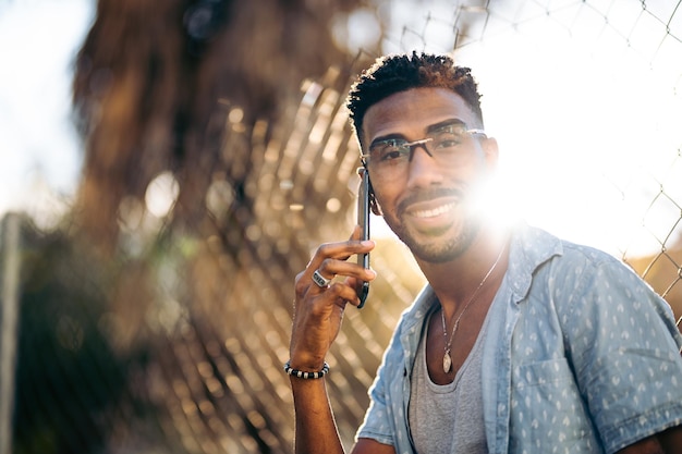 Ritratto di un bell'uomo afroamericano che usa il suo smartphone sorridente per strada guardando la fotocamera