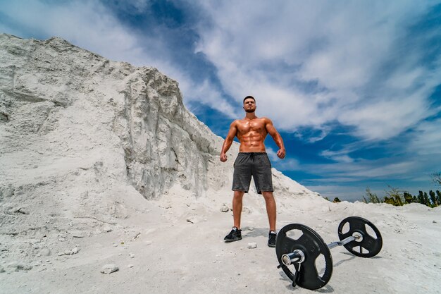 Ritratto di un bell'uomo bodybuilder seminudo con gli occhiali con manubri a terra. Uomo in posa. Corpo perfetto.