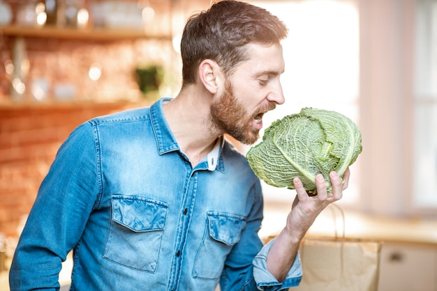 Ritratto di un bell'uomo che tiene la testa di cavolo in cucina. Concetto di cibo vegano sano