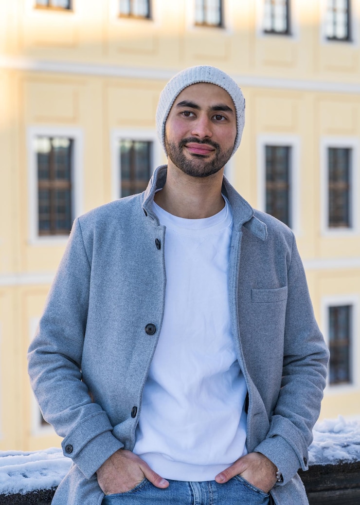 Foto ritratto di un bell'uomo giovane uomo asiatico sorridente con una barba ordinata che indossa un cappotto chiaro e un cappello bianco a maglia