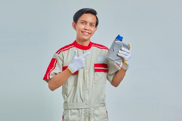 Ritratto di un bell'uomo sorridente che indossa l'uniforme del meccanico che mostra la bottiglia di plastica dell'olio motore su sfondo grigio