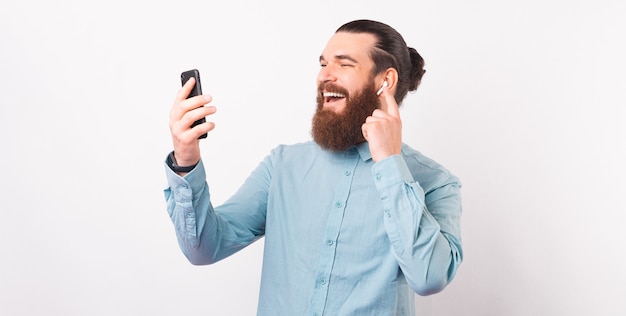 Ritratto di un bell'uomo sorridente che indossa una maglietta blu usando il telefono e gli auricolari