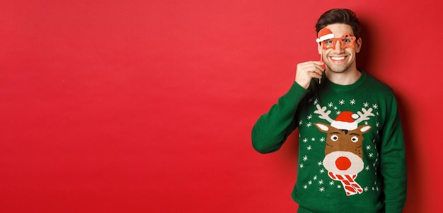 Ritratto di un bell'uomo sorridente in maglione natalizio e occhiali da festa che celebra il nuovo anno e ha...