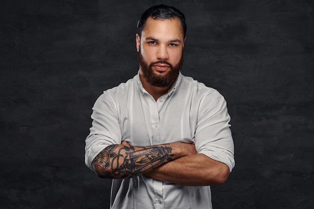 Ritratto di un bell'uomo tatuato afroamericano con capelli e barba alla moda, in piedi con le braccia incrociate. Isolato su uno sfondo scuro.