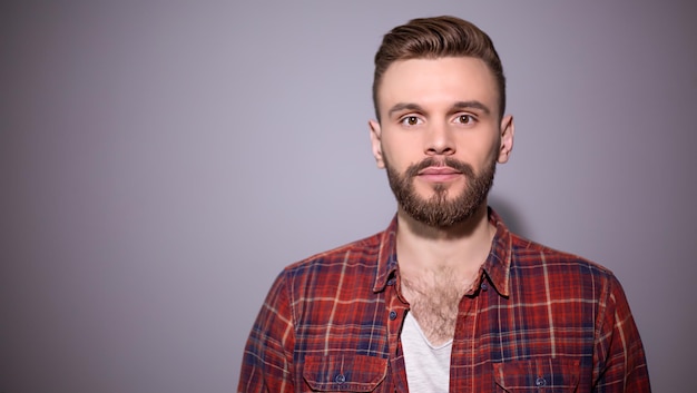 Ritratto di un bellissimo uomo barbuto sorridente in una camicia a scacchi rossa su sfondo grigio