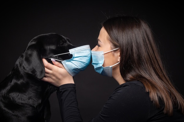 Ritratto di un cane Labrador Retriever in una maschera medica protettiva con un proprietario femminile