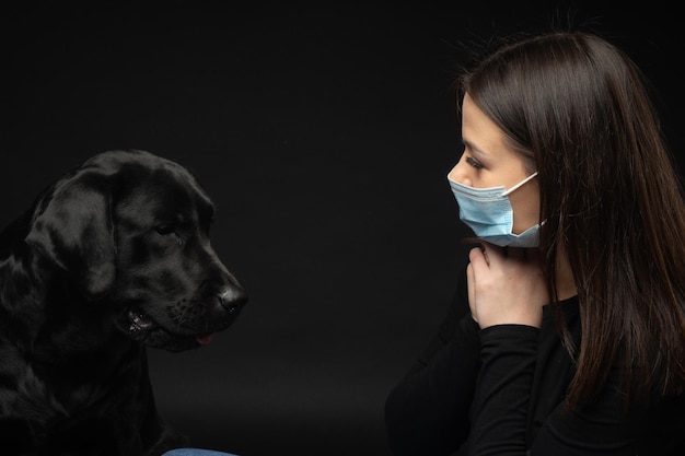Ritratto di un cane Labrador Retriever in una maschera medica protettiva con un proprietario femminile