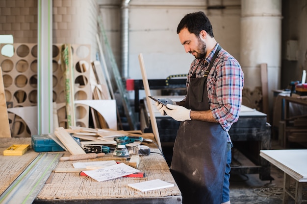 Ritratto di un carpentiere che sta nel suo studio della lavorazione del legno e che tiene compressa digitale