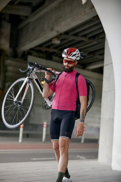 Ritratto di un ciclista in piedi sotto un ponte con una bicicletta in mano in posa davanti alla telecamera su uno sfondo di architettura Stile di vita attivo Il ciclismo è un hobby