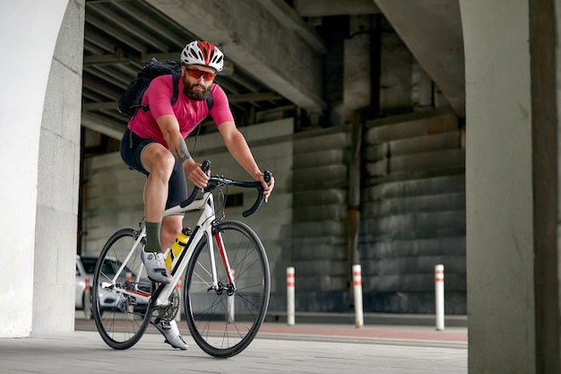 Ritratto di un ciclista in piedi sotto un ponte con una bicicletta in posa davanti alla telecamera su uno sfondo di architettura Stile di vita attivo Il ciclismo è un hobby