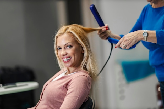 Ritratto di un cliente felice seduto in salone mentre il parrucchiere stira i capelli in un salone
