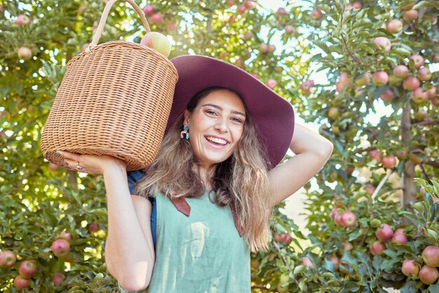 Ritratto di un contadino felice che tiene un cesto di mele appena raccolte in un frutteto fuori in una giornata di sole Donna allegra che raccoglie e raccoglie succosa frutta nutriente e biologica nella stagione estiva