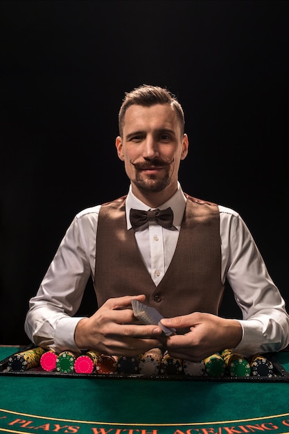 Ritratto di un croupier tiene in mano le carte da gioco fiches sul tavolo sfondo nero