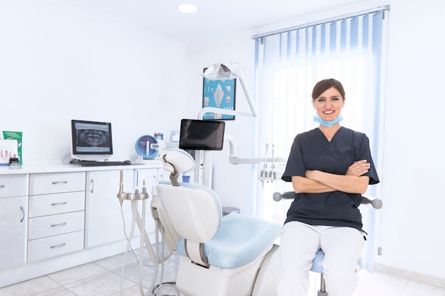 Ritratto di un dentista sicuro sorridente in clinica con macchina e attrezzature